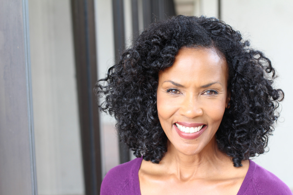 Mature woman with curly shoulder length hair smiling.