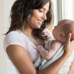 Close up of a mother with long brown hair holding her newborn baby.