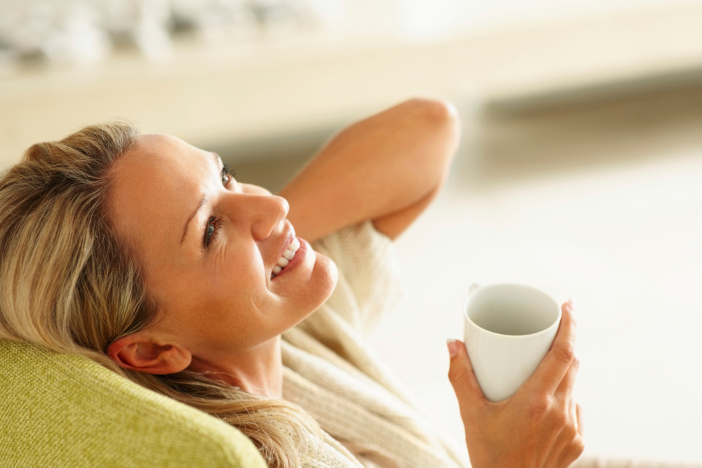 Woman relaxing on a green sofa with a cup of tea.