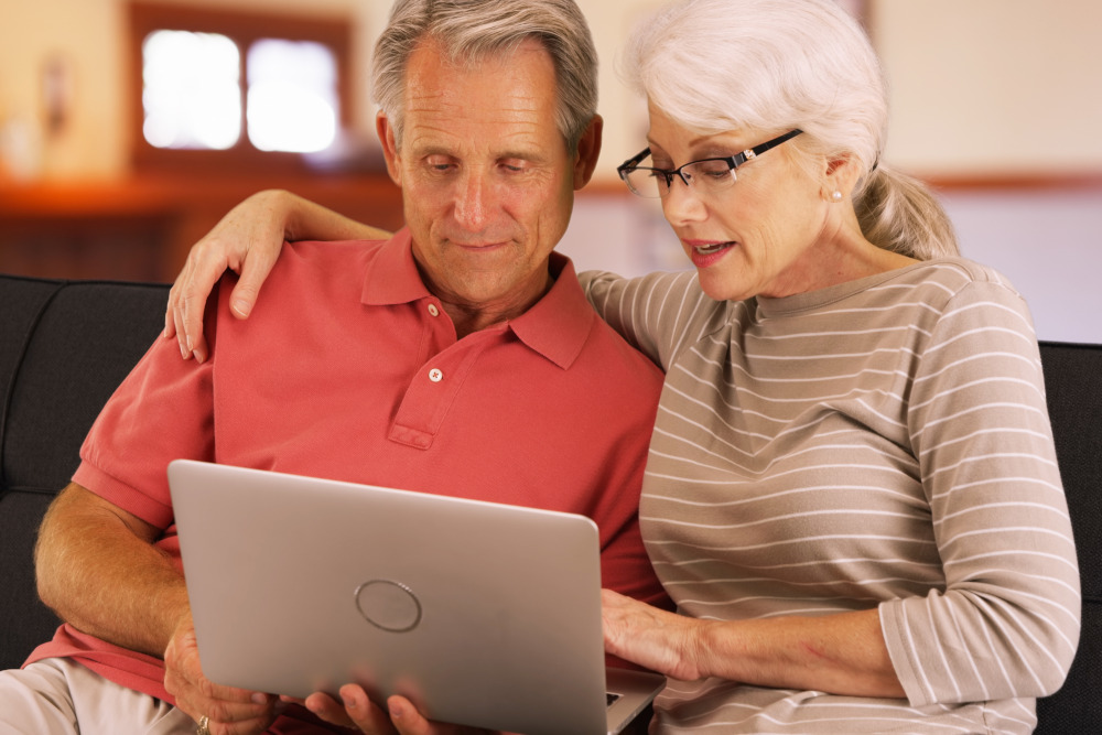 A mature man and woman sitting on the couch doing an internet search on their laptop for what to ask before getting a facelift.